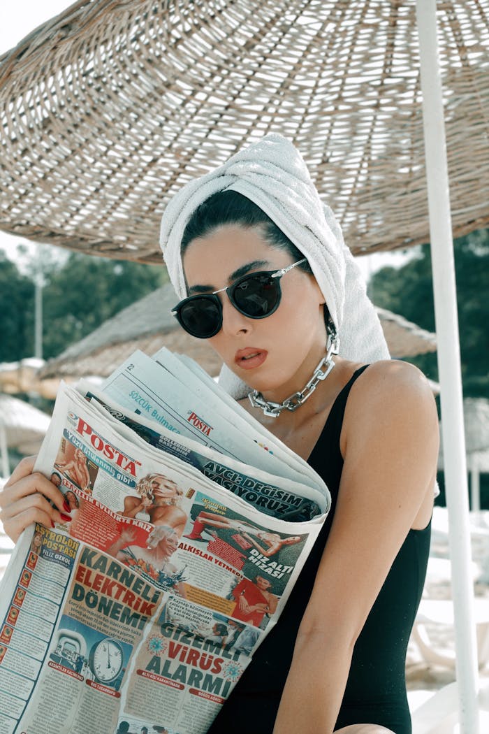 Woman in swimsuit with towel and sunglasses reads newspaper at a beach in Istanbul.